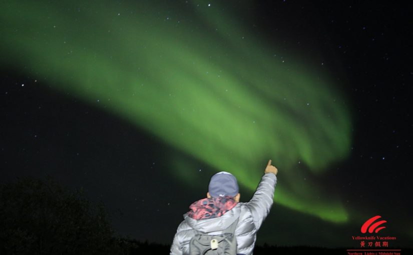A person gestures towards the vibrant northern lights illuminating the night sky with colorful displays.