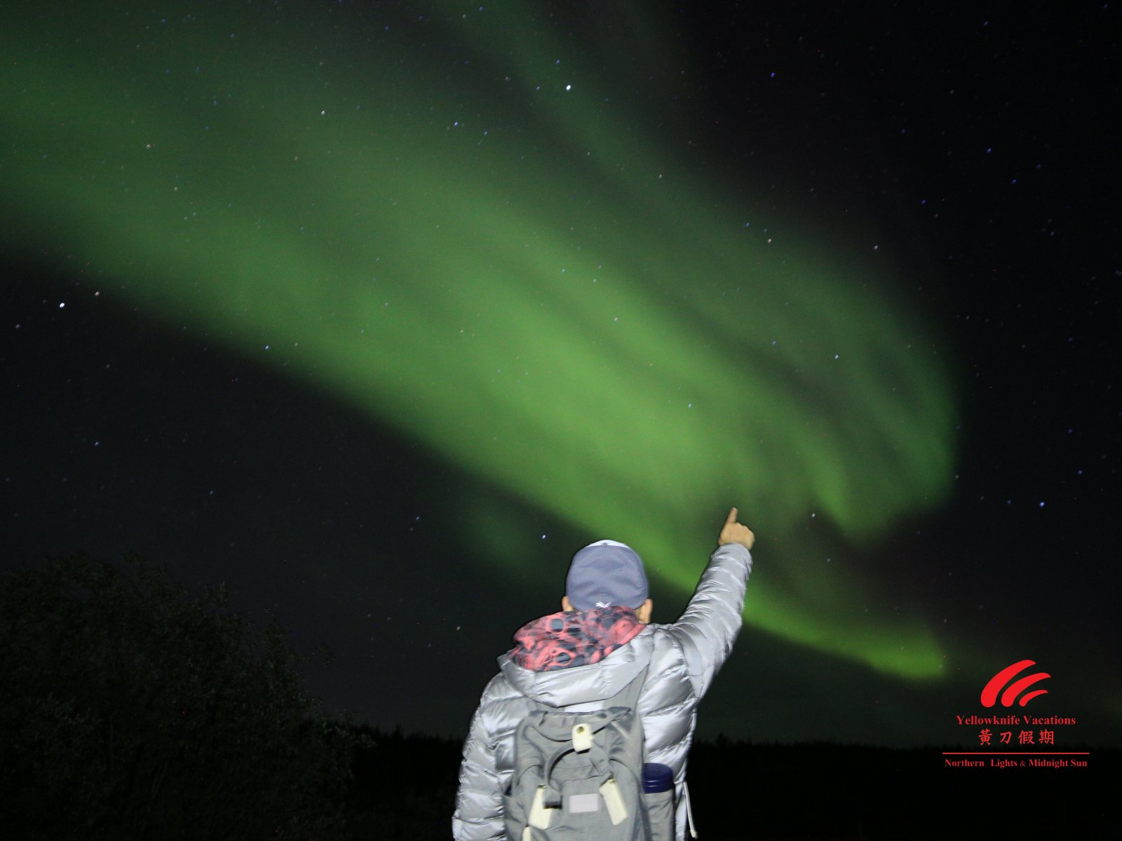 A person gestures towards the vibrant northern lights illuminating the night sky with colorful displays.